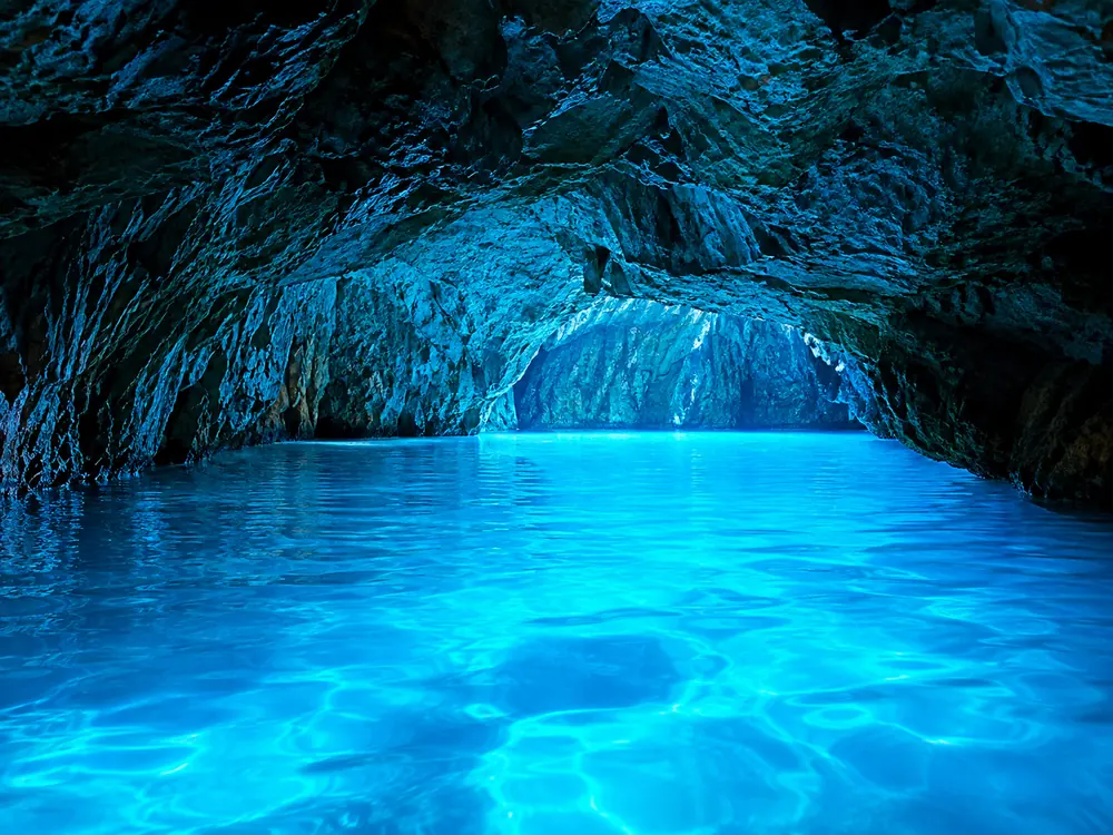 The interior of a sea cave lit blue from below the waterline