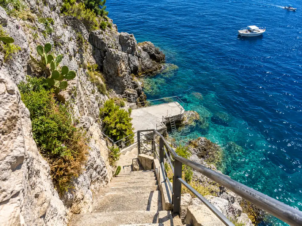 A flight of stairs dropping from a cliff road to a rowboat landing